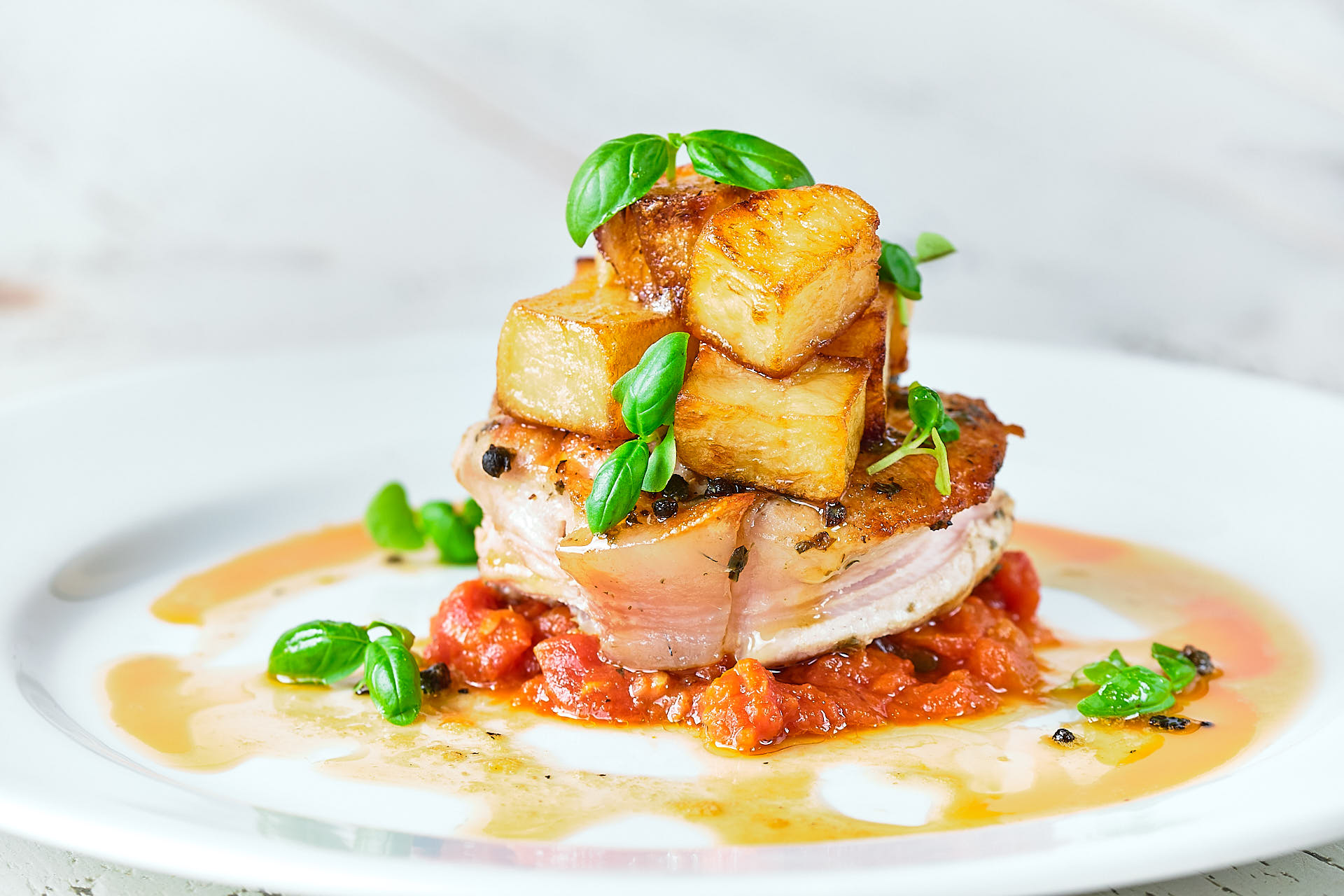 A tender slice of pork is served with roasted potatoes, a rich sauce and basil leaves.