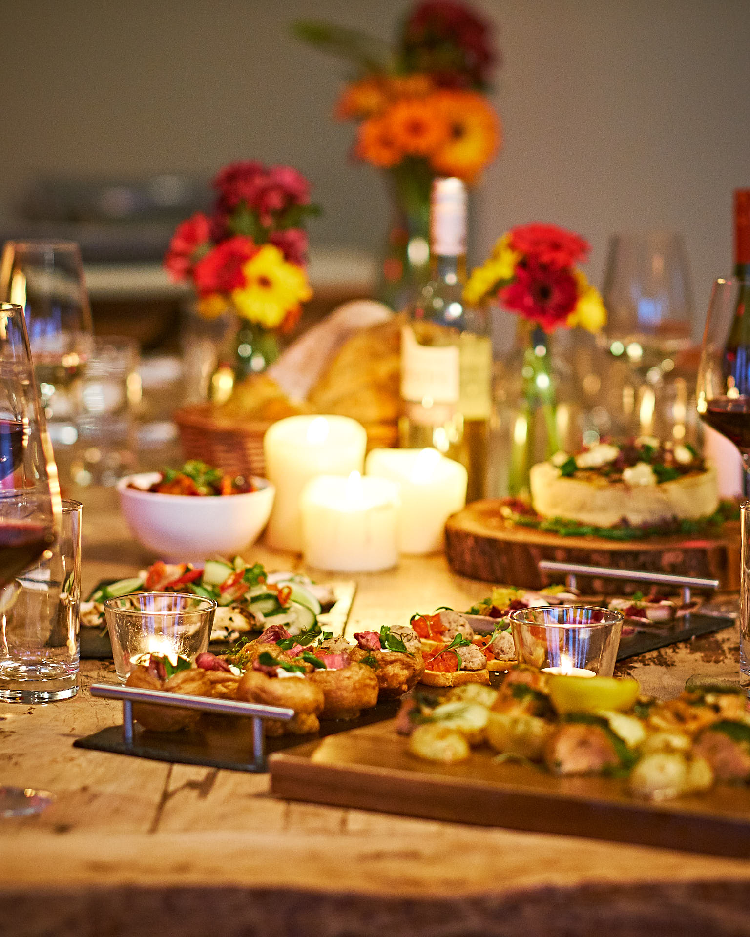 A candle-lit table filled with wooden platters of food to share at a party.
