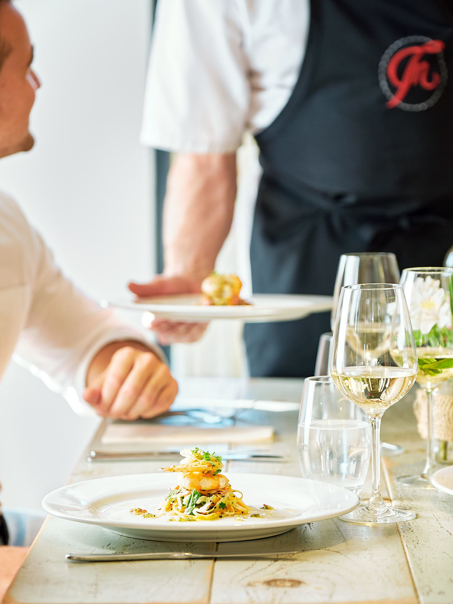 A chef brings food to to the table with a smiling customer looking up at him.